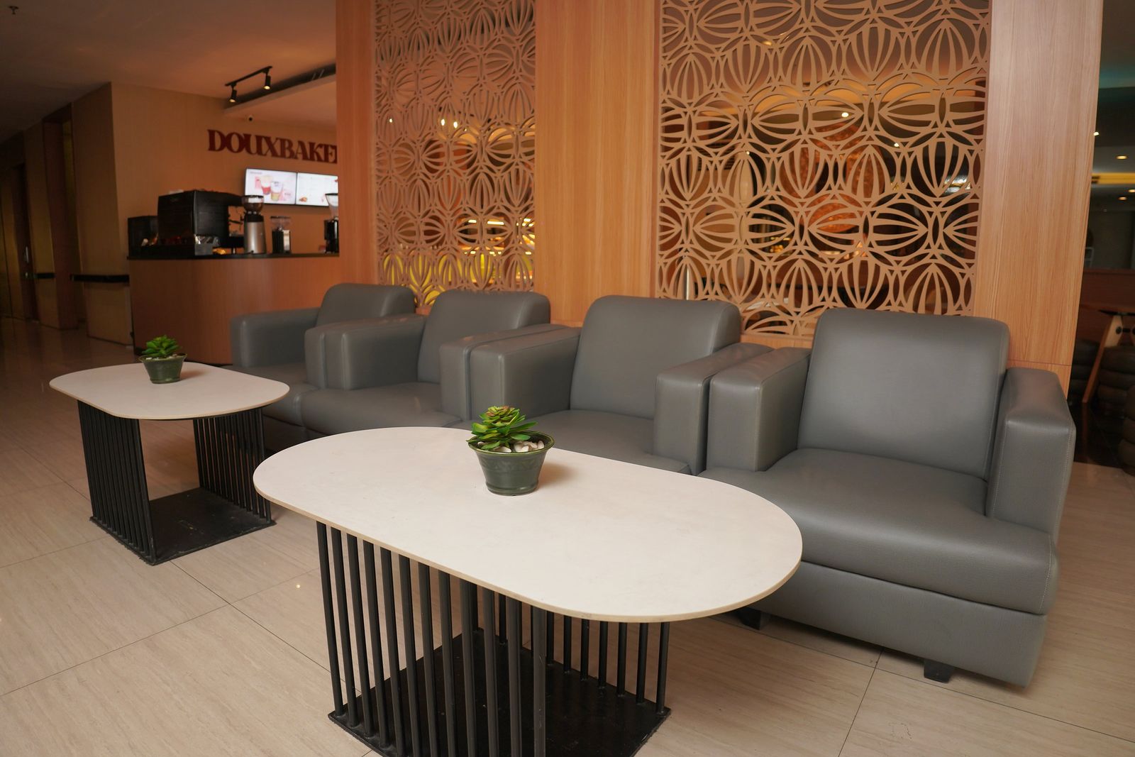 Area duduk lobby dengan sofa abu dan panel kayu berukir
