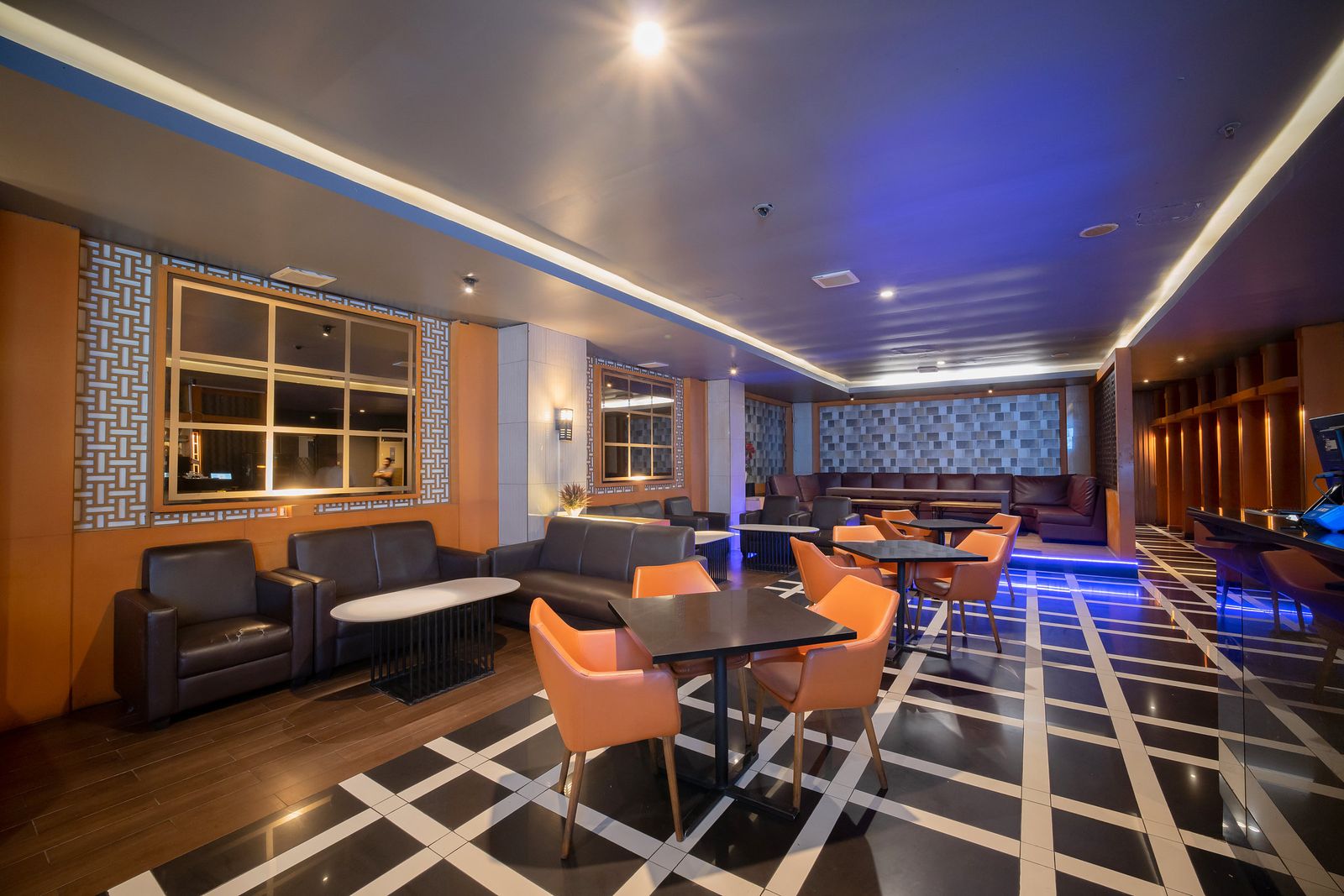 Area lounge hotel dengan kursi oranye, sofa kulit, dan lantai kotak hitam putih