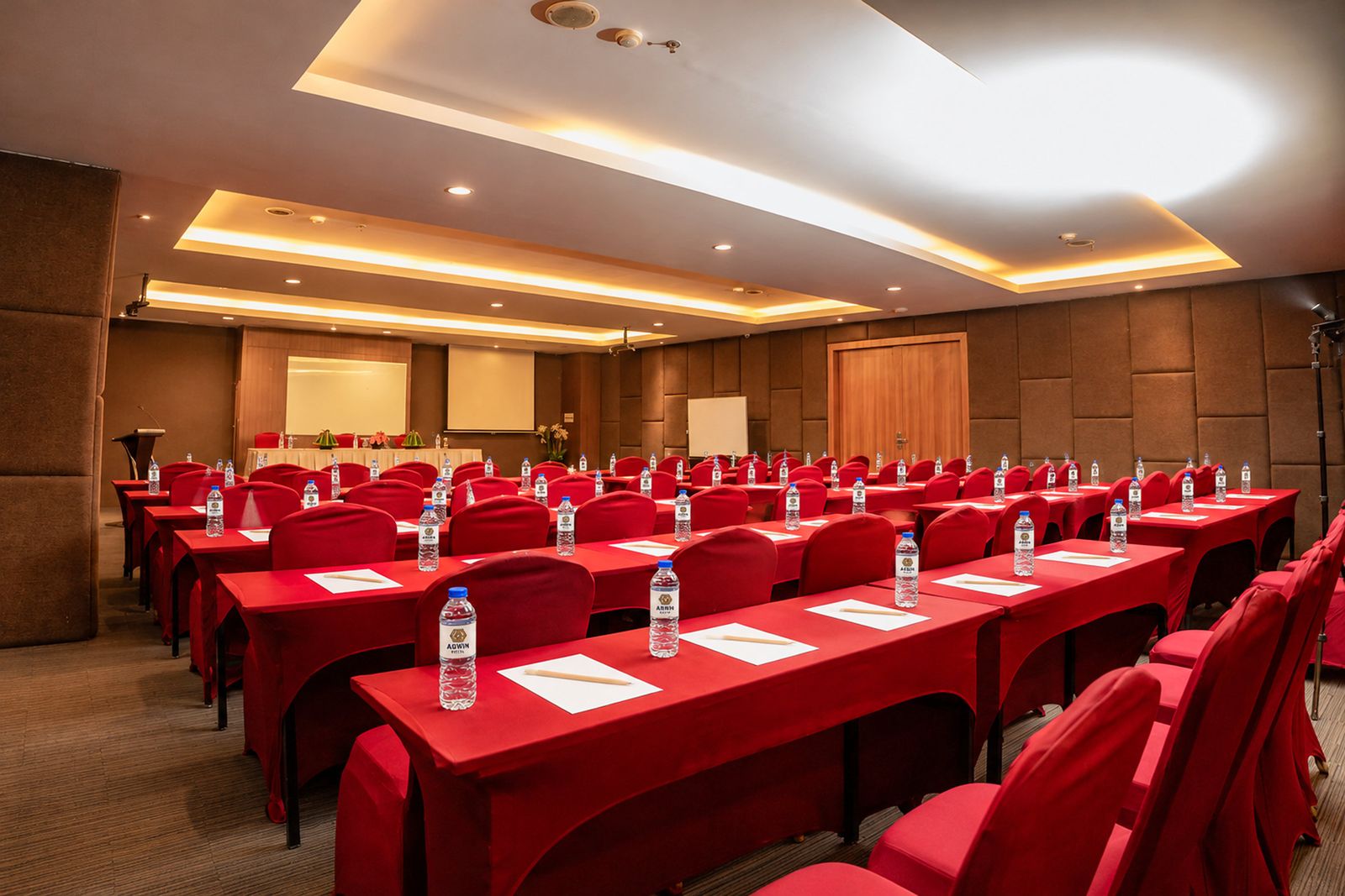 Ruang meeting dengan susunan classroom, meja bertaplak merah, dan layar proyektor